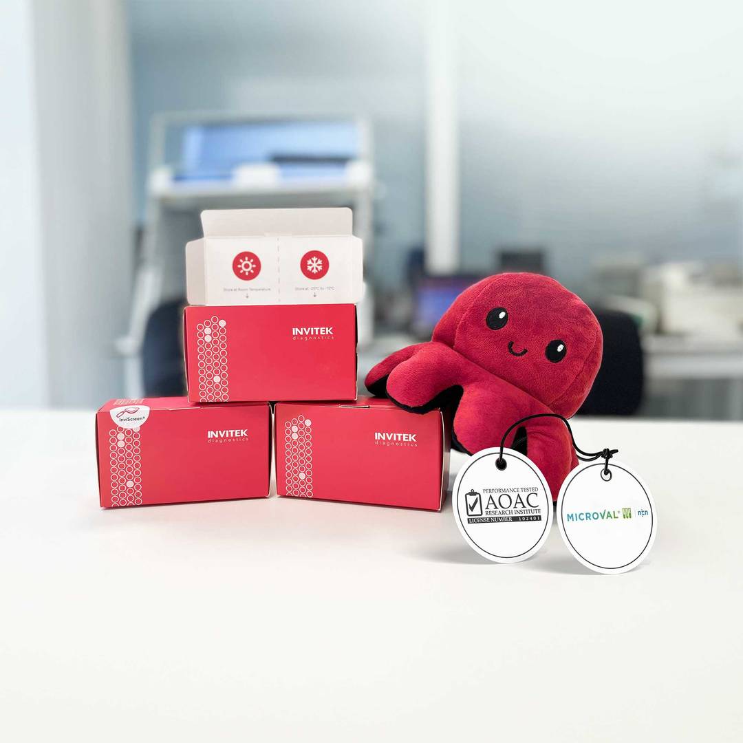 Three red and white boxes labeled 'INVITEK' stacked on a table, with an open box on top revealing its contents, next to a plush toy resembling an octopus with two medals.