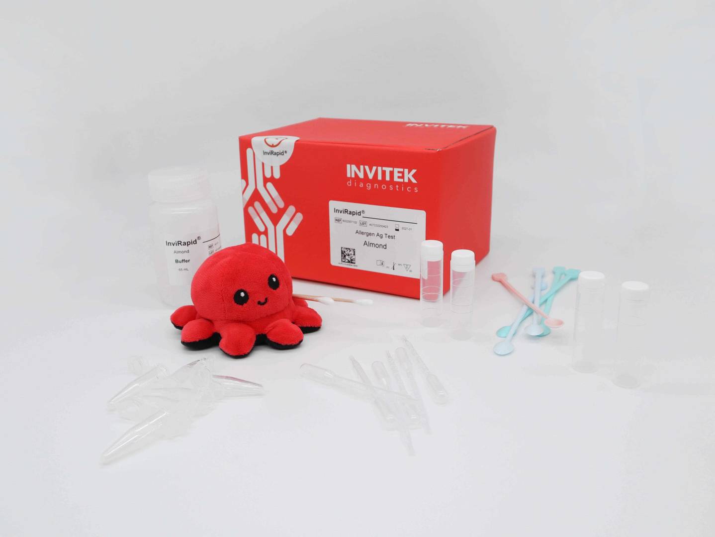Red Invitek Diagnostics InviRapid Almond Allergen Ag Test box behind a buffer bottle and sample tubes with scoops, droppers, swabs, and tubes laying scattered in front.