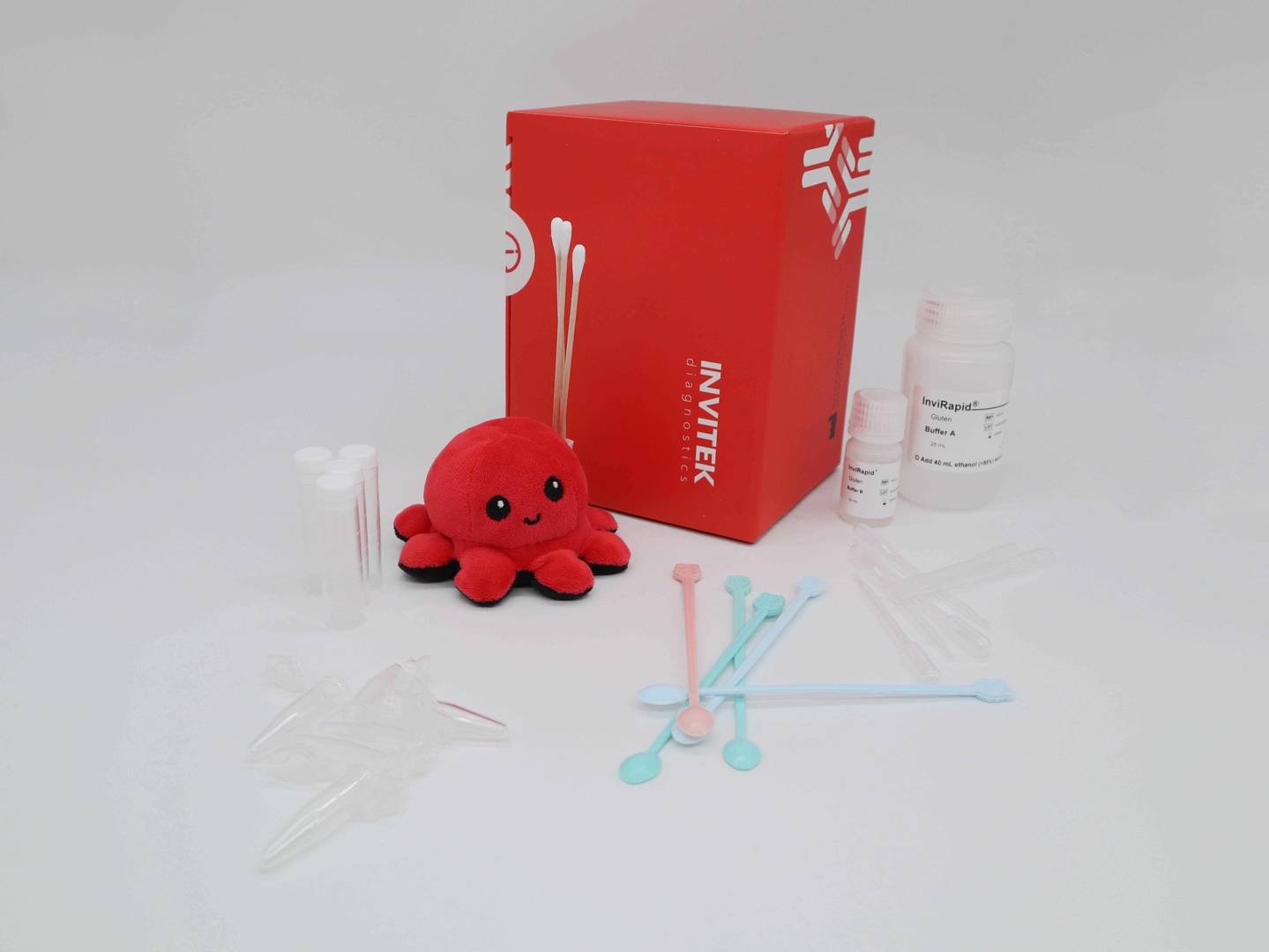 Red Invitek Diagnostics InviRapid Gluten Allergen Ag Test box behind swabs next to buffer bottles and sample tubes with scoops, droppers and tubes laying scattered in front.