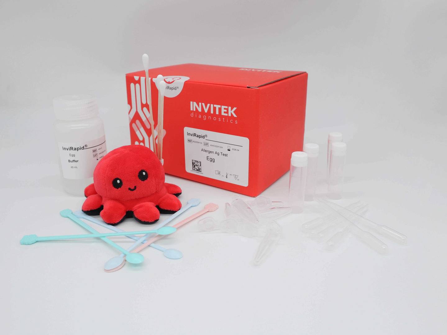 Red Invitek Diagnostics InviRapid Egg Allergen Ag Test box behind a buffer bottle, swabs, and sample tubes with scoops, droppers and tubes laying scattered in front.