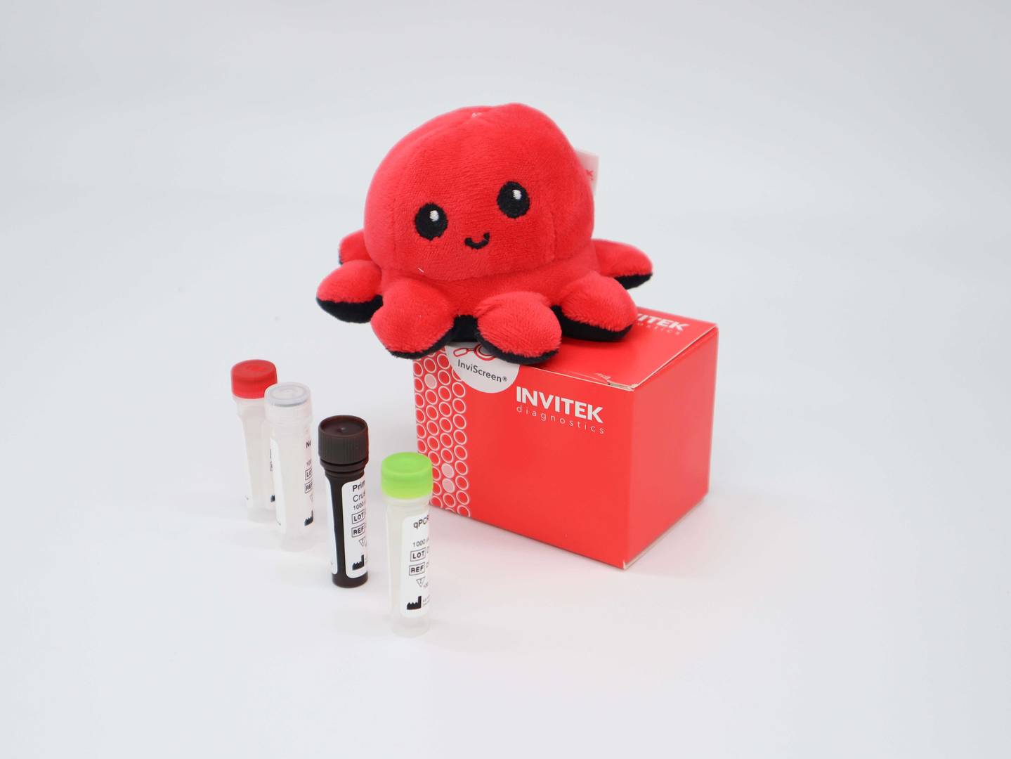 InviScreen IBV kit: plush red octopus “Invi” perched on a red INVITEK box; four reagent vials (red, grey, brown, green caps) stand in front on a white surface.