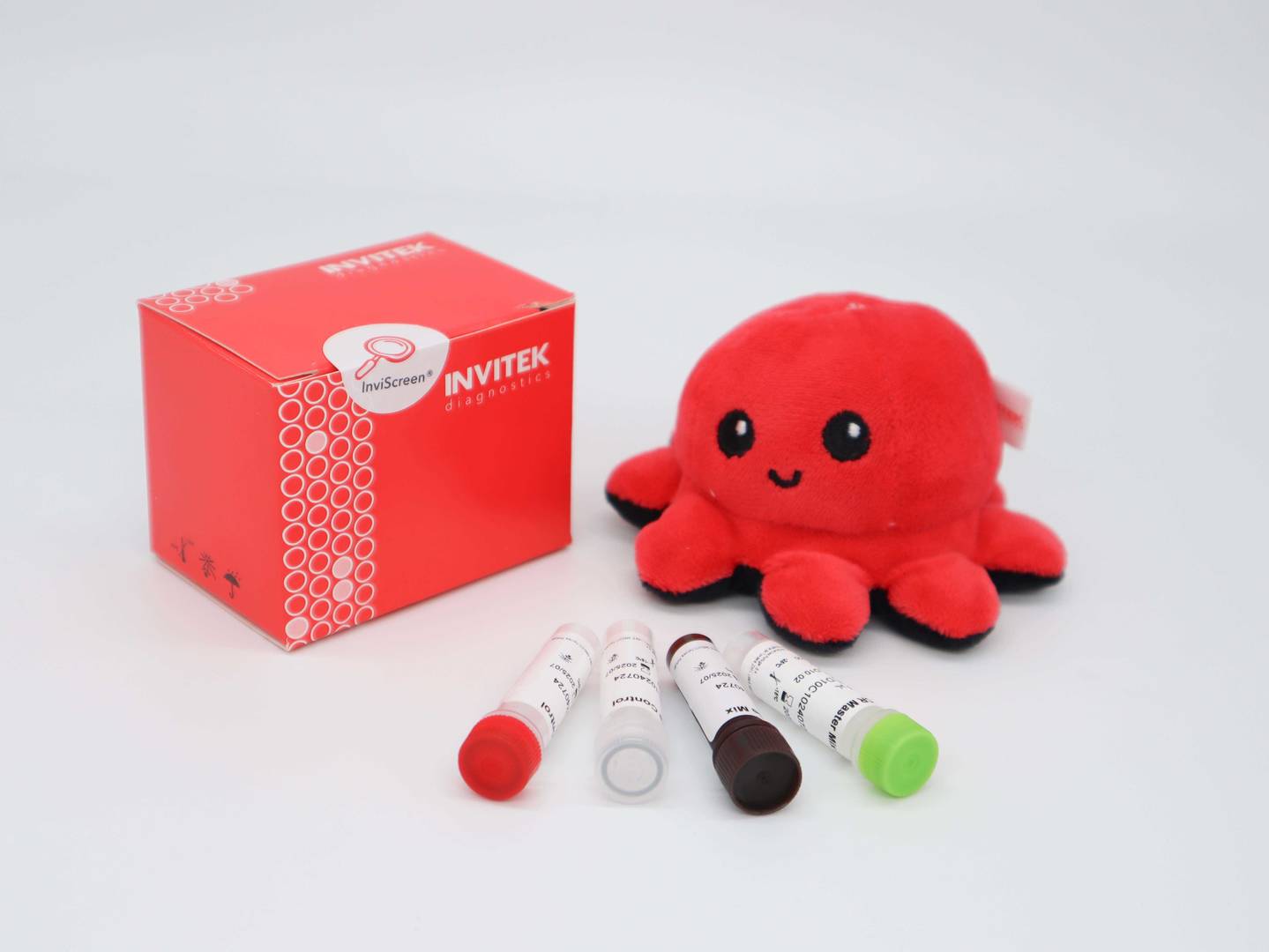 InviScreen O157:H7 kit: red box at left, plush octopus to the right, and five reagent vials (red, grey, brown, green and clear caps) spread in front.