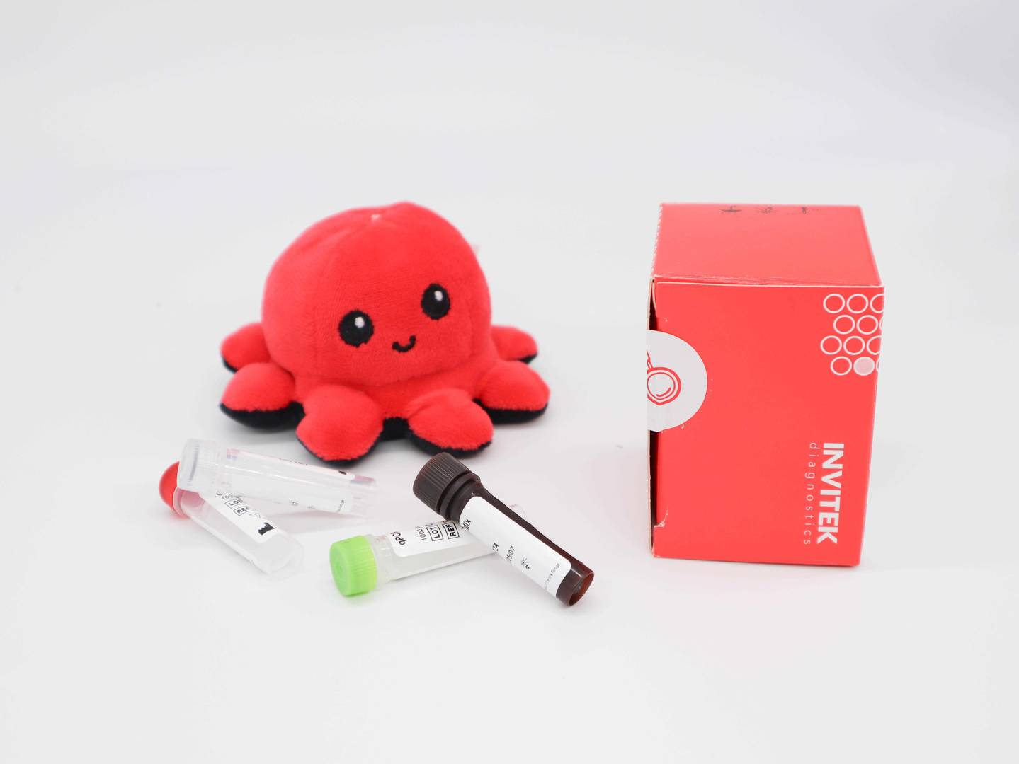 InviScreen SARS-CoV-2 4G kit: plush octopus beside red INVITEK box, with mixed reagent vials (clear, green, brown caps) lying in foreground.