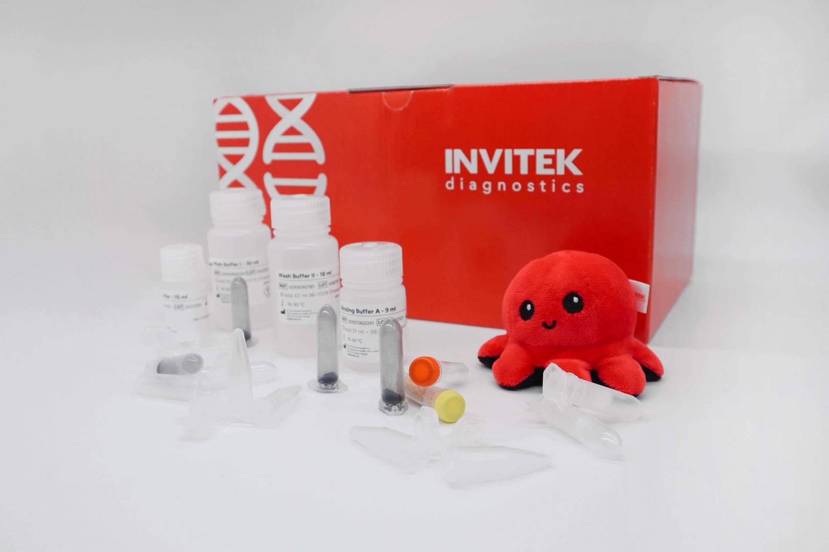 Red Invitek Diagnostics PSP Spin Stool DNA Basic Kit box behind reagent bottles, color-coded reagent vials, and tubes laying scattered in front.